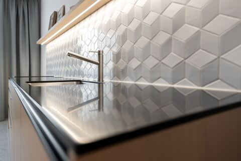 Detail kuchynskej batérie na tmavej pracovnej doske pred bielym geometrickým obkladom
